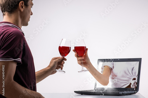 Handsome man toasting a wine glasses with her online date coming through her laptop screen. photo