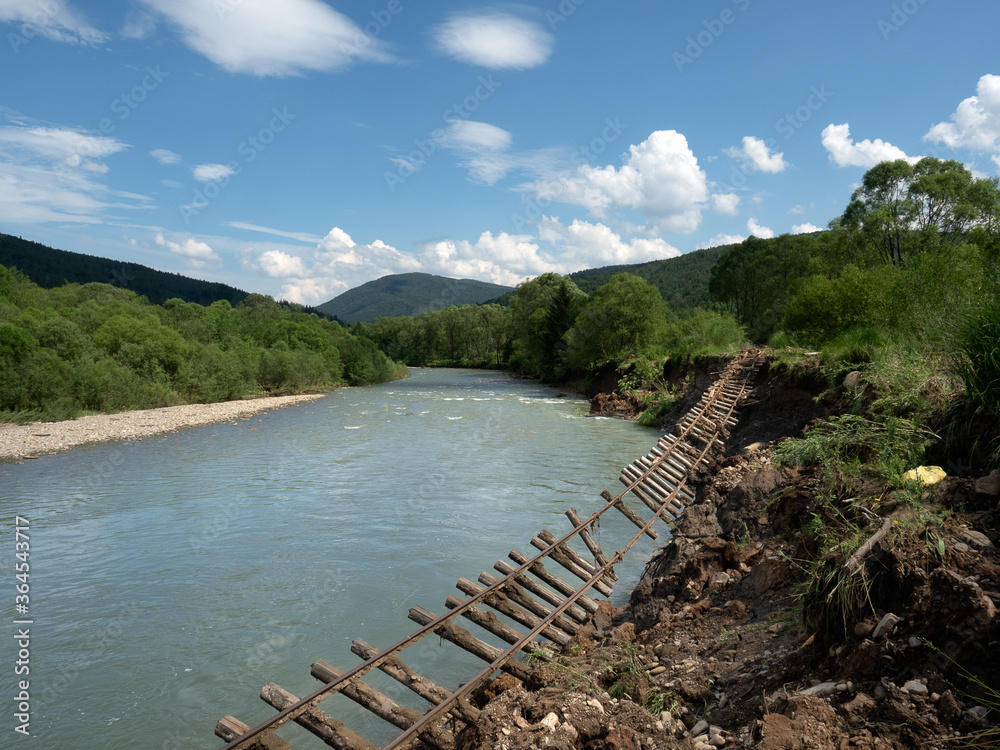 Damaged section of 750 mm old historic narrow gauge railway track hanging near a cliff near Vyhoda, Carpathian Mountains, Ukraine, along Mizunka River, built during Austria-Hungary. Soft focus Damaged section of 750 mm old historic narrow gauge railway track hanging near a cliff near Vyhoda, Carpathian Mountains, Ukraine, along Mizunka River, built during Austria-Hungary. Soft focus