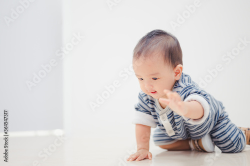 Smiling crawling asian baby boy at home on floor with white background.