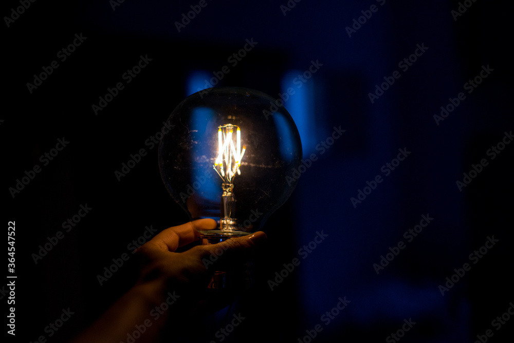 Big filament bulb with yellow light on blue background. Large LED lamps in retro style. Close up glowing light bulb. Round glowing tungsten lamp. Decorative antique tungsten light bulb. Copy space