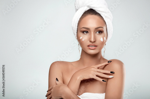Portrait of a charming girl with a towel on her head and smears of cream on her cheeks. Personal care. Spa and relaxation. Copy space. Studio photo