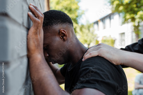 selective focus of policeman detaining african american man on street, racism concept
