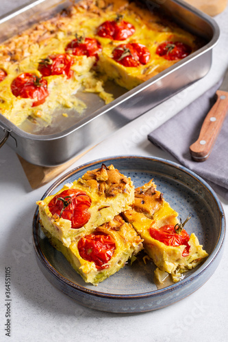 Vegetable clafoutis on gray plate on concrete background, savory pie with cabbage and whole cherry tomatoes. Vegetarian cuisine.
