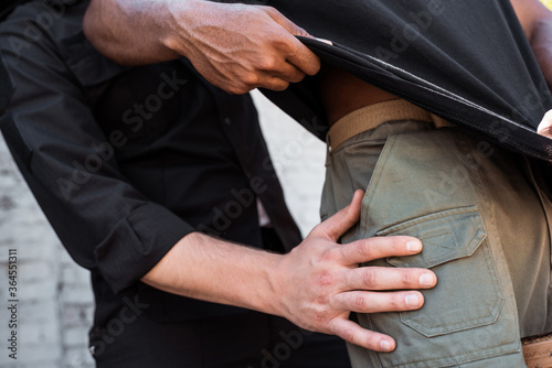 cropped view of policeman touching clothing of african american man