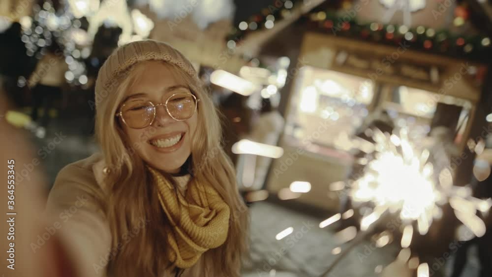 Gorgeous blonde smiling and burning bright sparklers on New Year's Eve. Selfie time, girl blogger is making video and photo for her social page at the street fair on the central Square of Prague.