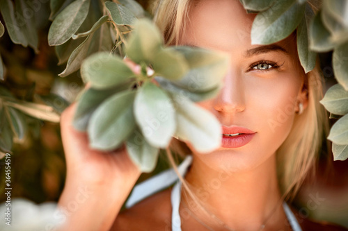 Portrait of a blonde with natural beauty among the leaves of tropical trees. Spa and pleasure