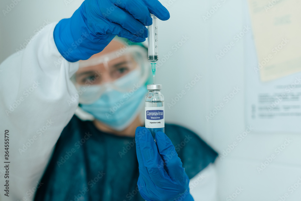 Young female medical specialist in protective mask and gloves filing syringe with vaccine from vial for prevention and immunization from coronavirus infection