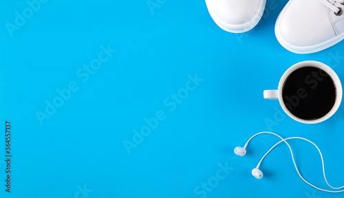 Fitness concept. Coffee, white sneakers and earphones on blue background. Sports flat lay. Concept healthy lifestyle. Top view. Copy space. Banner.