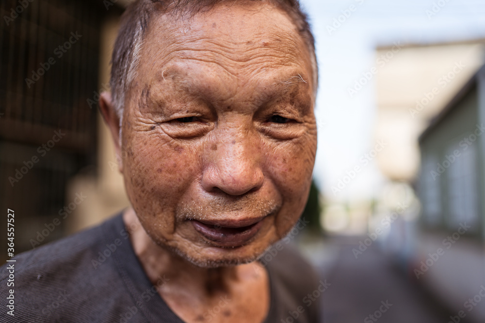Portrait of elderly Asian male gardener in casual clothes smiling at camera while standing on street in settlement in Taiwan Portrait of elderly Asian male gardener in casual clothes smiling at camera while standing on street in settlement in Taiwan