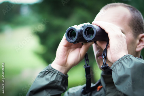 A young hunter in the forest looks into the binoculars. He is trying to find some wild animals.