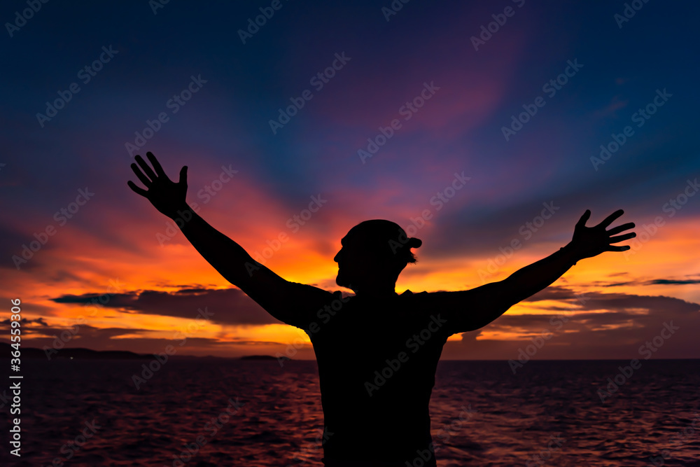 silhouette of a man with hands up on sunset background