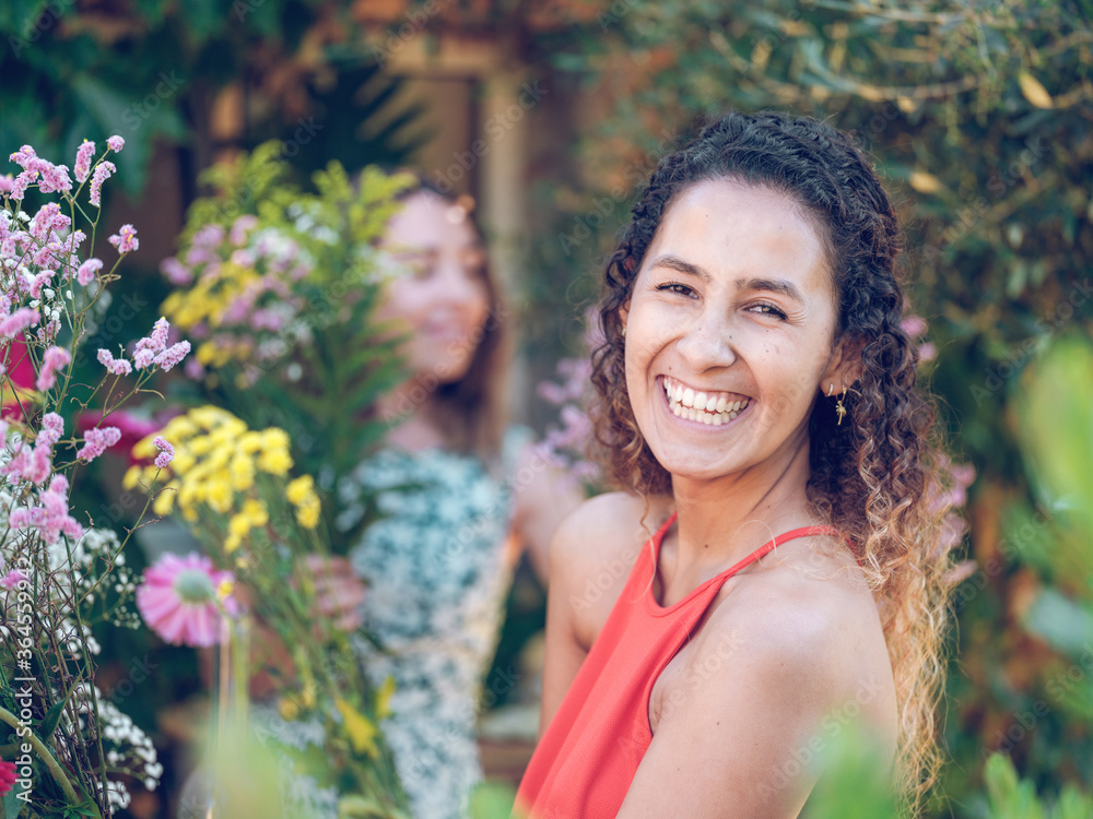 Side view of charming young lady cheerfully smiling and looking at camera while standing near amazing flowers Side view of charming young lady cheerfully smiling and looking at camera while standing near amazing flowers