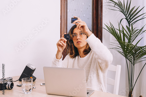 Young female photographer sitting at table with laptop and photo camera with projector and working with old photo slides at home workplace