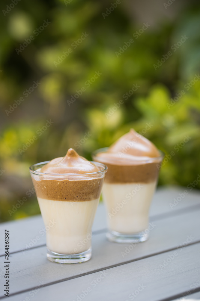 Whipped coffee Dalgona coffee in cold milk on wooden table surface with green plants on the background Whipped coffee Dalgona coffee in cold milk on wooden table surface with green plants on the background