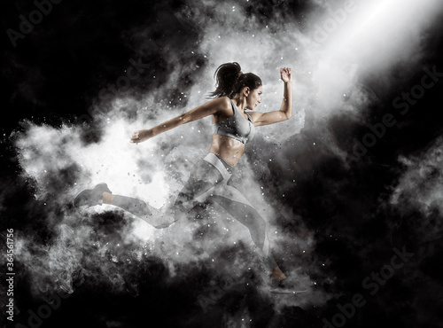 Obraz na plátně Sporty young woman running on smoke background