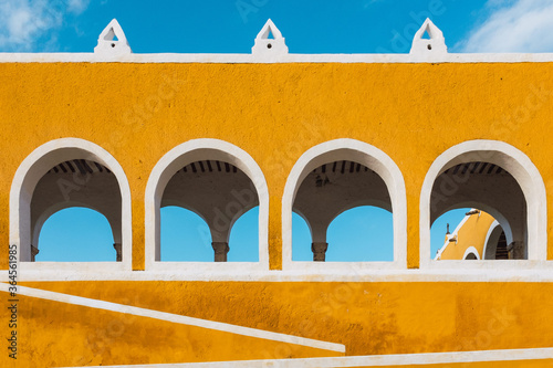 Exterior of vivid yellow walls with arches in ancient city of Izamal against blue sky photo