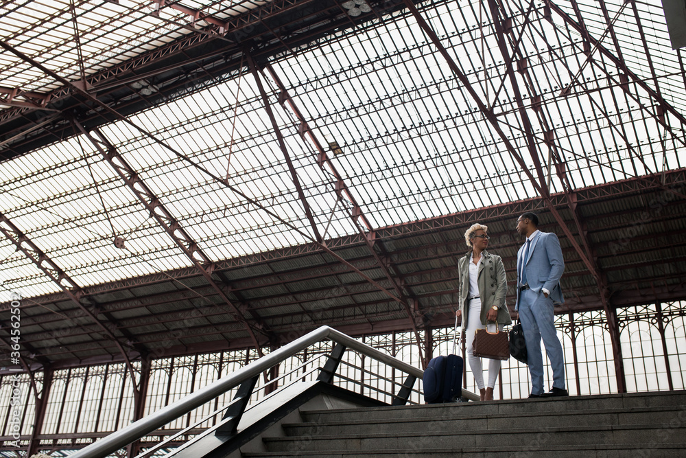 Elegant black woman and man having talk while walking down stairs on railway station. Elegant black woman and man having talk while walking down stairs on railway station.