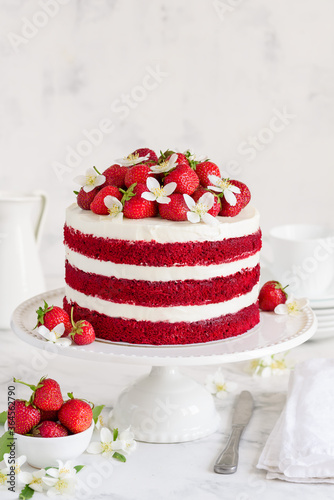 Red velvet cake decorated with strawberries and jasmine flowers on a white stand. Selective focus photo