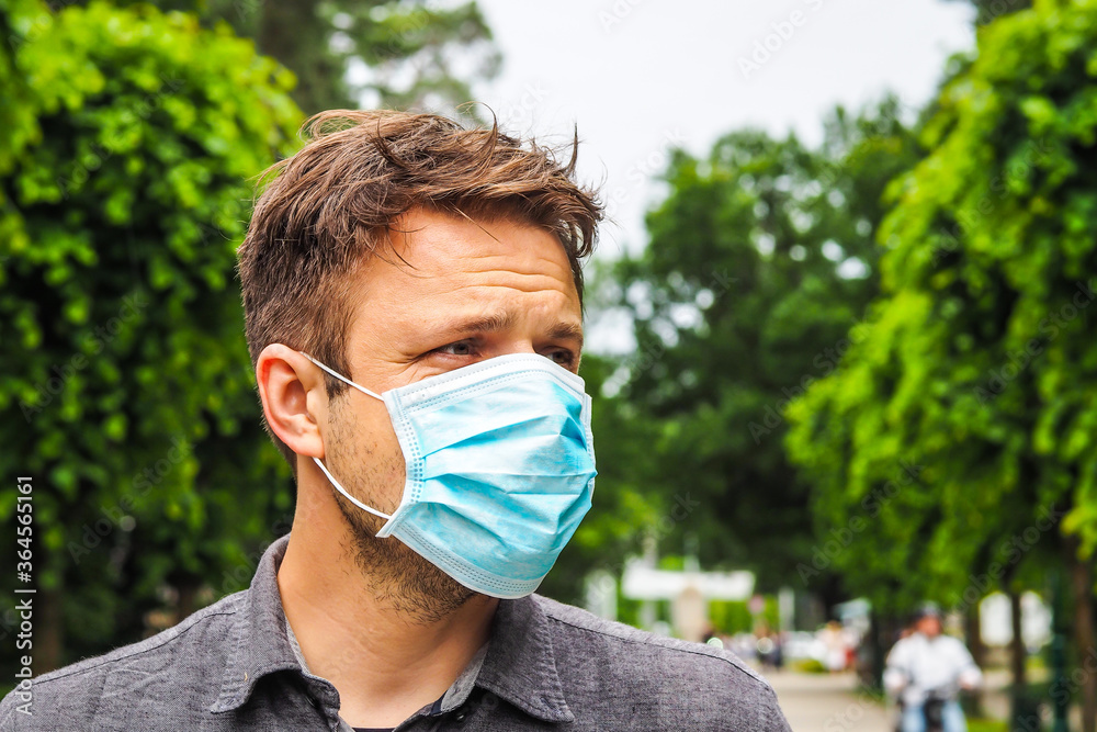 Handsome young European man in a park with a medical face mask on. Closeup of a 35-year-old male in a respirator to protect against coronavirus Handsome young European man in a park with a medical face mask on. Closeup of a 35-year-old male in a respirator to protect against coronavirus