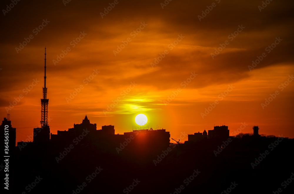 Sunset in the Kyiv with silhouette of high rise buildings, skyscrapers and TV tower on orange sky