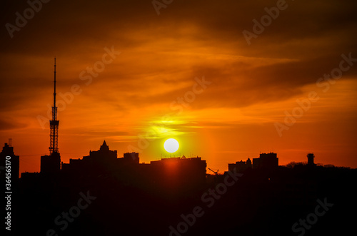 Sunset in the Kyiv with silhouette of high rise buildings, skyscrapers and TV tower on orange sky