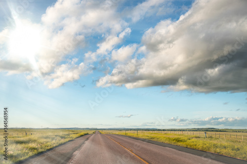 Amazing road across the countryside at sunset, blue sky with clouds and grass