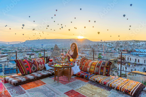 A woman have breakfast on one of the Cappadocia roof in early morning sunrise, when balloons fly. Romantic scene Cappadocia, Turkey..