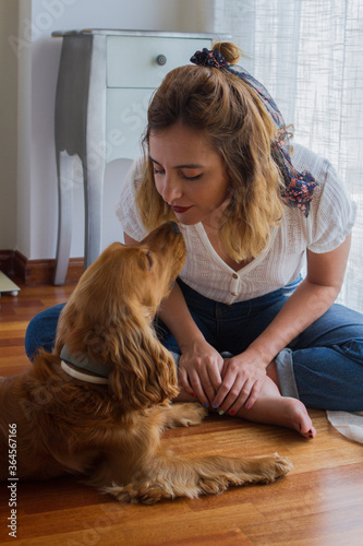 Chica joven con pañuelo en el pelo sentada en el suelo de madera de su habitación mirando a su perro de cerca