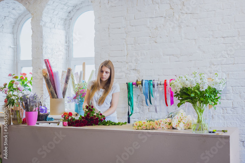 Professional woman floral artist, florist making beautiful fresh wedding bouquet, floral composition in white bright room of workshop, flower shop. Floristry, decor, handmade , small business concept