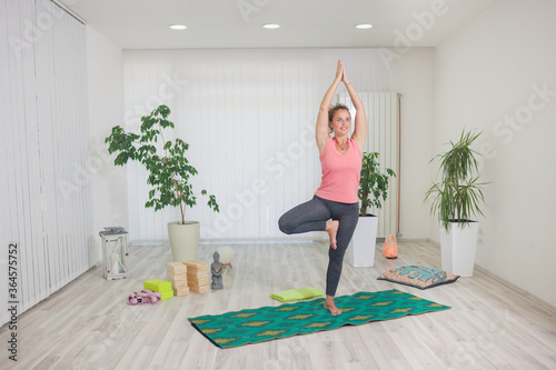 one young middle aged woman practising yoga, indoors in yoga studio, Vrikshasana (Tree Pose).