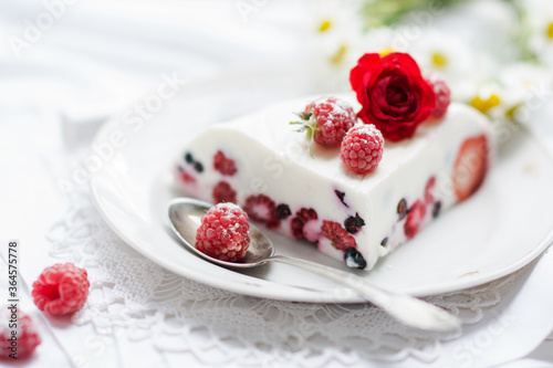 Dessert of yogurt , berries and gelatin, decorated with raw raspberries and natural red rose in white background, fresh, healthy food 