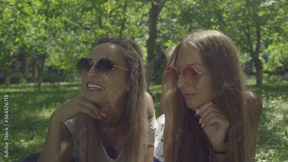 Naklejka premium Two beautiful young women in sunglasses are lie on green grass