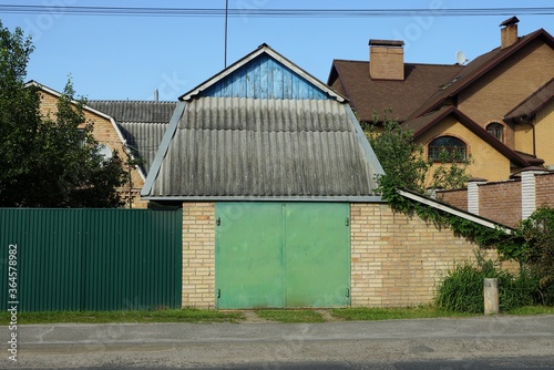brown brick garage with green iron gates under a gray slate roof on a rural street