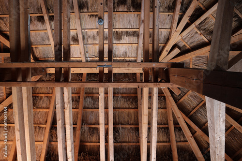 View of wooden beams and construction of roof covered by hay from inside the hut