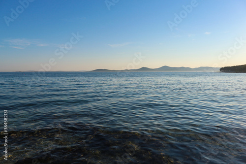 Peaceful, crystal clear, blue adriatic sea at sunset off the Pakostane town shore, with rows of islands in the distance on the horizon