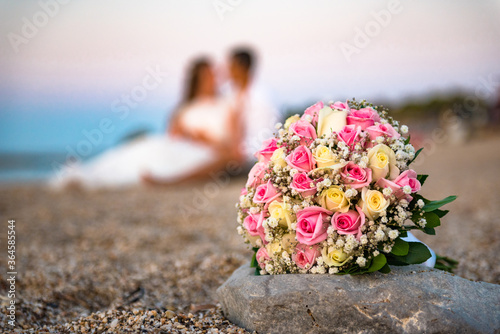 Wedding flower bouquet on the stone on the beach, at the blurred background beach,sea and couple in love.