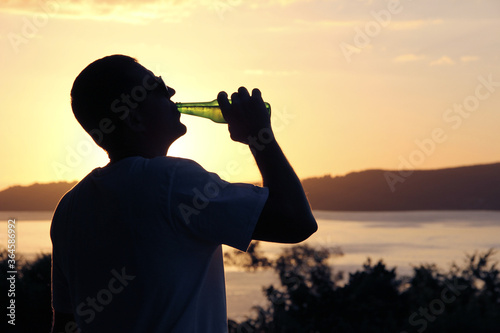Fényképezés Silhouette of a man drinking beer from a bottle on a background of a lake and su