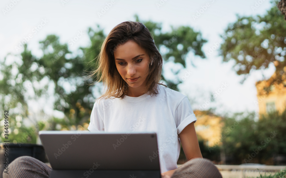caucasian hipster girl using tablet outdoors, cheerful young freelancer working on touch pad at green park, female student studying sitting grass with laptop computer outside caucasian hipster girl using tablet outdoors, cheerful young freelancer working on touch pad at green park, female student studying sitting grass with laptop computer outside