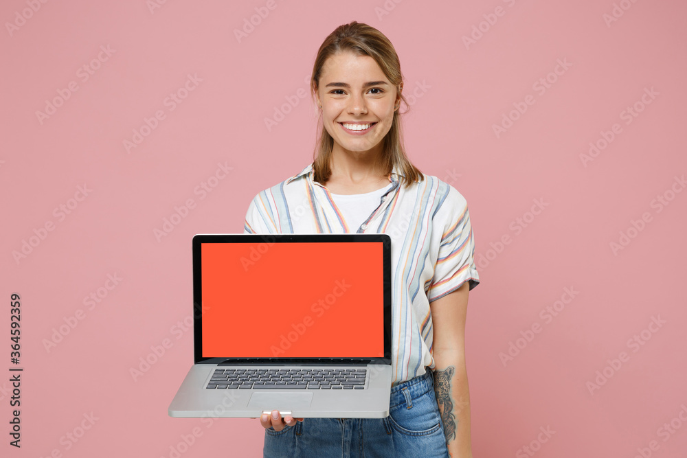 Smiling young blonde woman girl in casual striped shirt posing isolated on pastel pink background studio. People lifestyle concept. Mock up copy space. Hold laptop pc computer with blank empty screen. Smiling young blonde woman girl in casual striped shirt posing isolated on pastel pink background studio. People lifestyle concept. Mock up copy space. Hold laptop pc computer with blank empty screen.