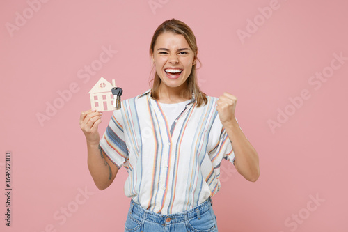Happy young blonde woman girl in casual striped shirt posing isolated on pastel pink background studio. People lifestyle concept. Mock up copy space. Hold house, bunch of keys, doing winner gesture.