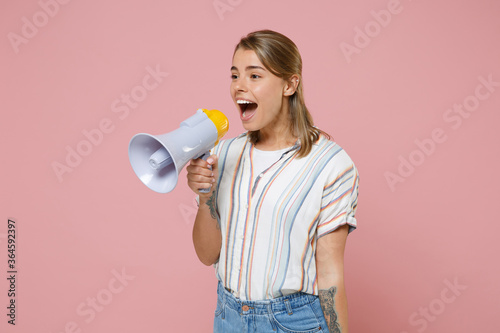 Excited young blonde woman girl in casual striped shirt posing isolated on pastel pink background studio portrait. People lifestyle concept. Mock up copy space. Screaming in megaphone, looking aside.