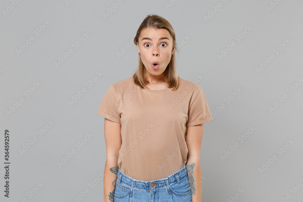 Shocked young blonde woman girl in casual beige t-shirt posing isolated on gray wall background studio portrait. People sincere emotions lifestyle concept. Mock up copy space. Keeping mouth open. Shocked young blonde woman girl in casual beige t-shirt posing isolated on gray wall background studio portrait. People sincere emotions lifestyle concept. Mock up copy space. Keeping mouth open.