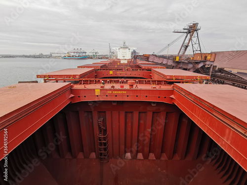 View of bulk carrier main deck with opened hatch-covers, cargo holds during loading of iron ore concentrate in bulk photo