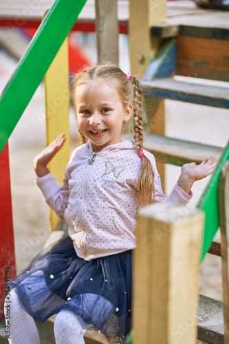 The girl sits on the steps of the house in the playground and smiles. girl in a light blouse and dark skirt