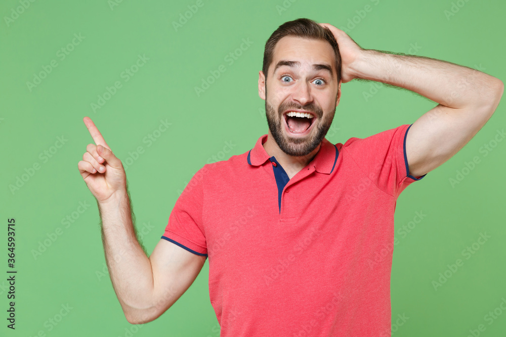 Excited young bearded man guy in casual red pink t-shirt posing isolated on green background studio portrait. People lifestyle concept. Mock up copy space. Point index finger up, put hand on head. Excited young bearded man guy in casual red pink t-shirt posing isolated on green background studio portrait. People lifestyle concept. Mock up copy space. Point index finger up, put hand on head.