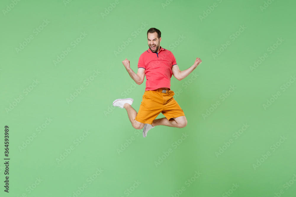 full length Happy young bearded man guy in casual red pink t-shirt posing isolated on green wall background studio portrait. People lifestyle concept. Mock up copy space. Jumping, doing winner gesture full length Happy young bearded man guy in casual red pink t-shirt posing isolated on green wall background studio portrait. People lifestyle concept. Mock up copy space. Jumping, doing winner gesture