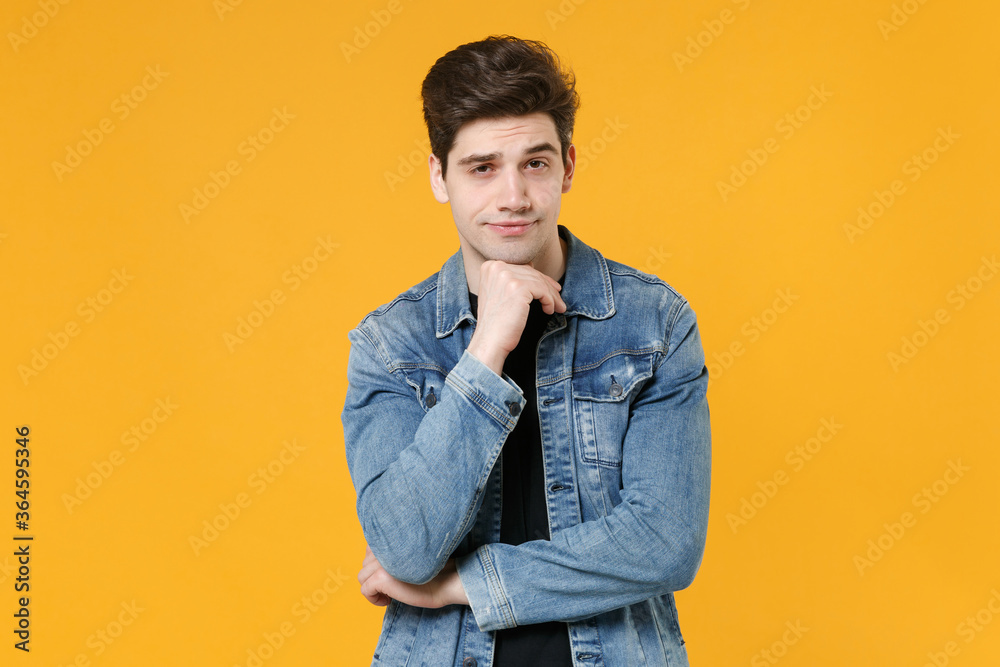 Attractive young man guy wearing casual denim jacket posing isolated on yellow wall background studio portrait. People sincere emotions lifestyle concept. Mock up copy space. Put hand prop up on chin. Attractive young man guy wearing casual denim jacket posing isolated on yellow wall background studio portrait. People sincere emotions lifestyle concept. Mock up copy space. Put hand prop up on chin.
