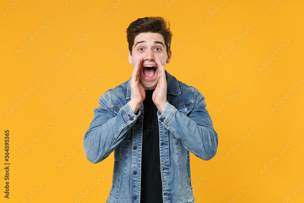Excited young man guy in casual denim jacket posing isolated on yellow background studio portrait. People sincere emotions lifestyle concept. Mock up copy space. Scream with hands gesture near mouth.