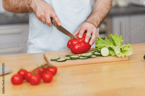 Cropped image of young man guy in white casual t-shirt posing preparing vegetable salad cooking food in light kitchen at home. Dieting healthy lifestyle concept. Mock up copy space.
