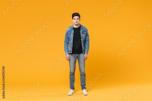 full length Attractive young man guy 20s in casual denim clothes posing isolated on yellow wall background studio portrait. People sincere emotions lifestyle concept. Mock up copy space. Look camera.
